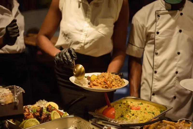Personal i svarta handskar lägger upp ris från en buffé med grillat kött, lime och stekt ris