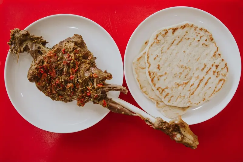 Kryddat, långkokt lammlägg med chili och örter bredvid grillade tunnbröd på röd botten