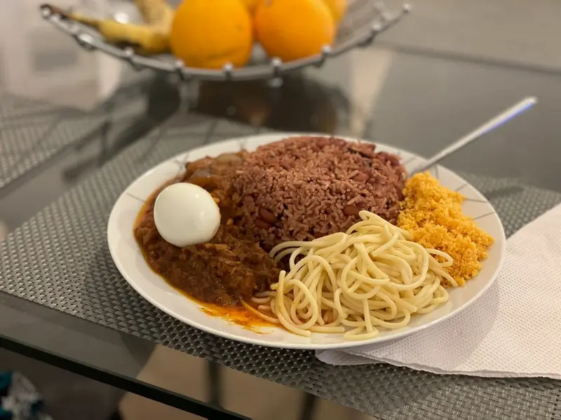 Waakye, ris och bönor, med tomatgryta, kokt ägg, spaghetti och gari på vit tallrik